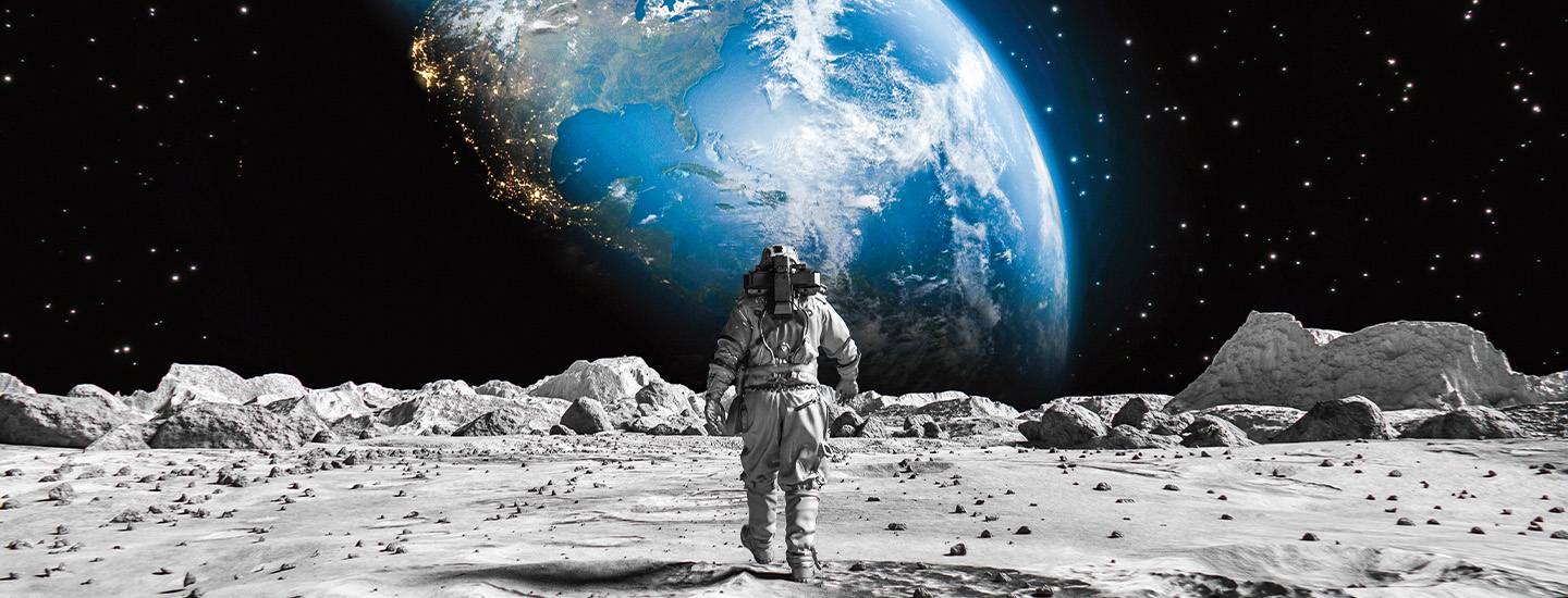 An astronaut stands on the lunar surface and faces Earth rising above the horizon