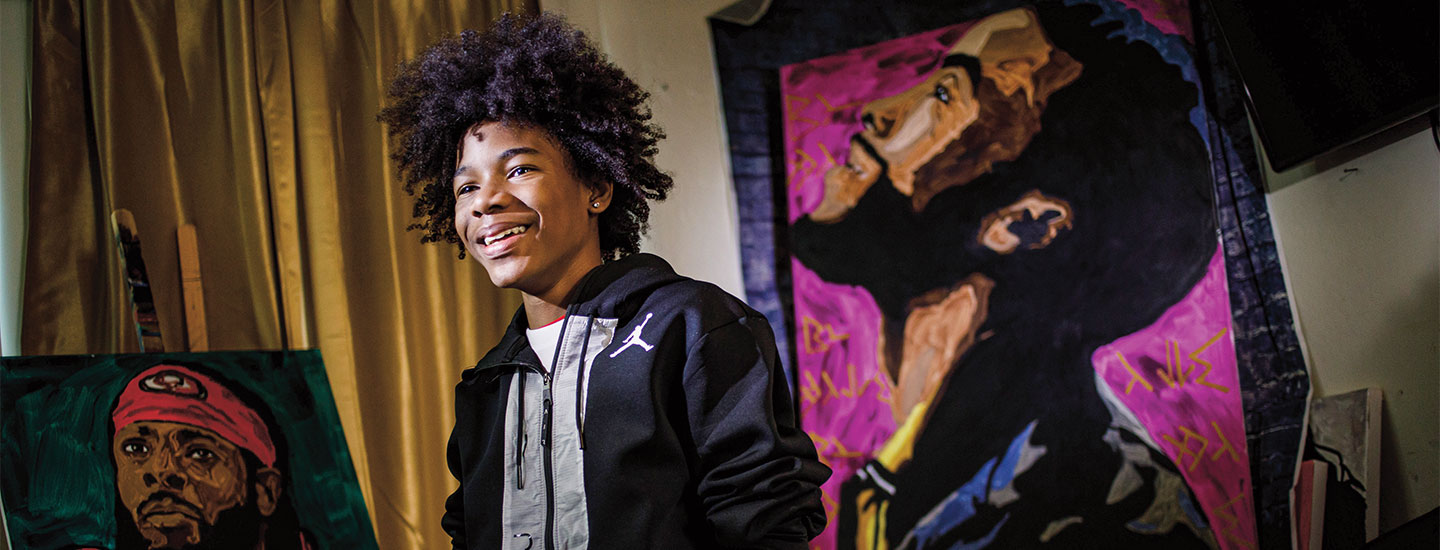 a boy smiling while standing in front of painted portraits